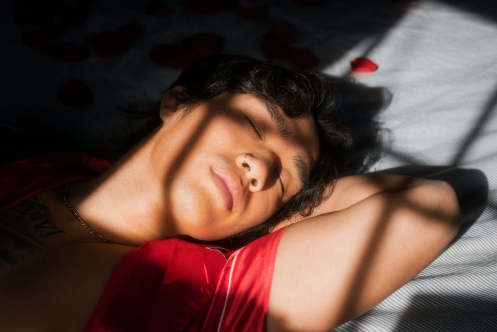 Selbstfürsorge Tipps: Guter Schlaf - ein junger Mensch liegt entspannt auf dem Bett. Es ist das Gesicht und die geschlossenen Augen zu sehen.